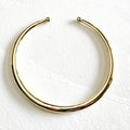 A polished gold hoop collar necklace with a small ball detail at each end, displayed on a textured white fabric background.