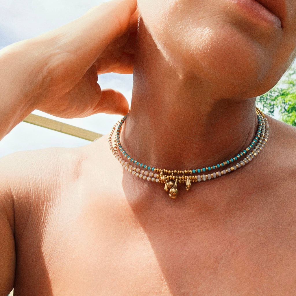 Close-up of a person wearing a beaded necklace with a blurred outdoor background