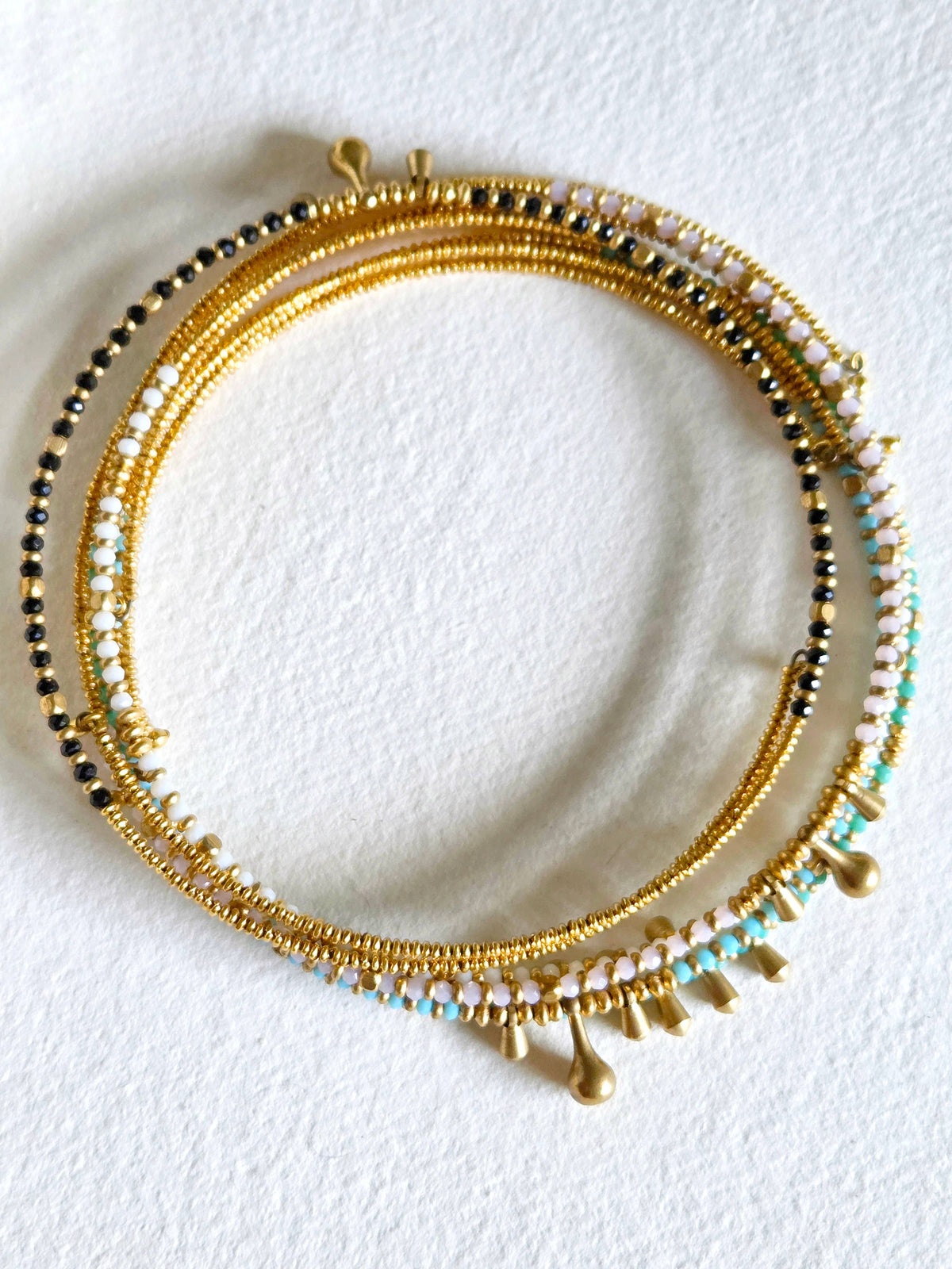 Gold beaded bracelet with black and blue beads on a white background