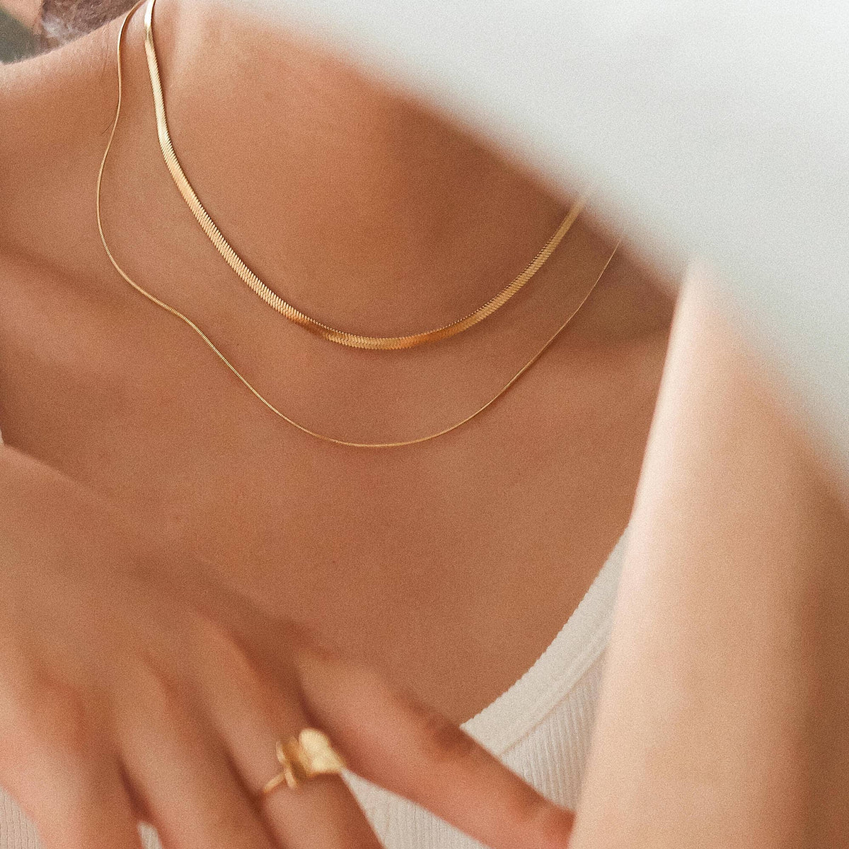 Gold necklace and ring on a person against a neutral background