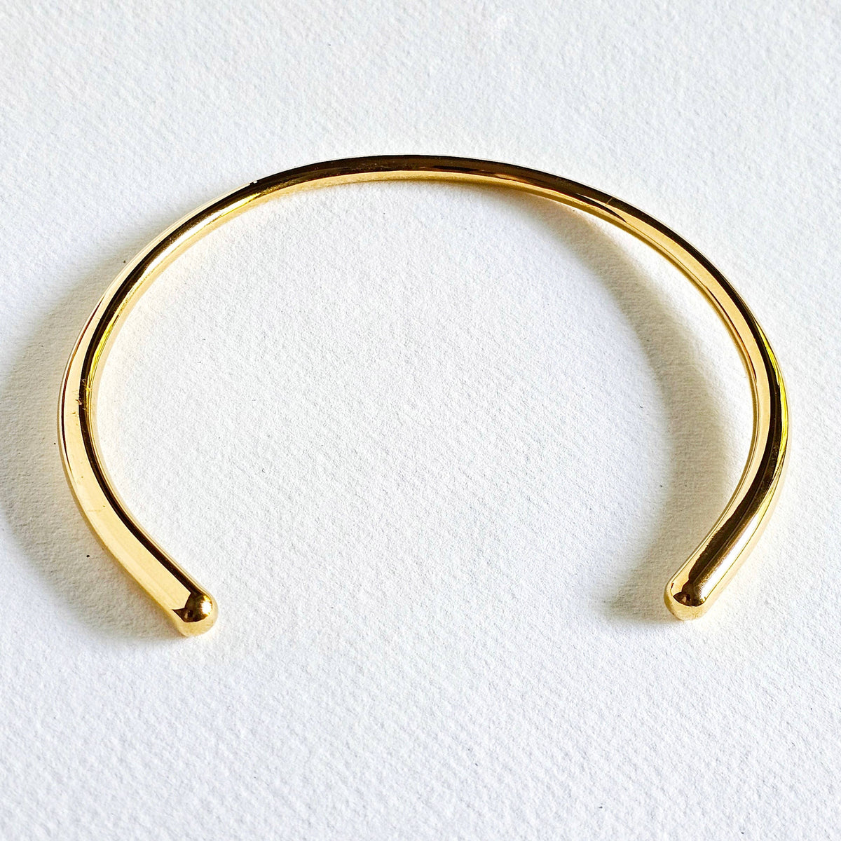 A minimalist style collar necklace, photographed on a textured white surface.