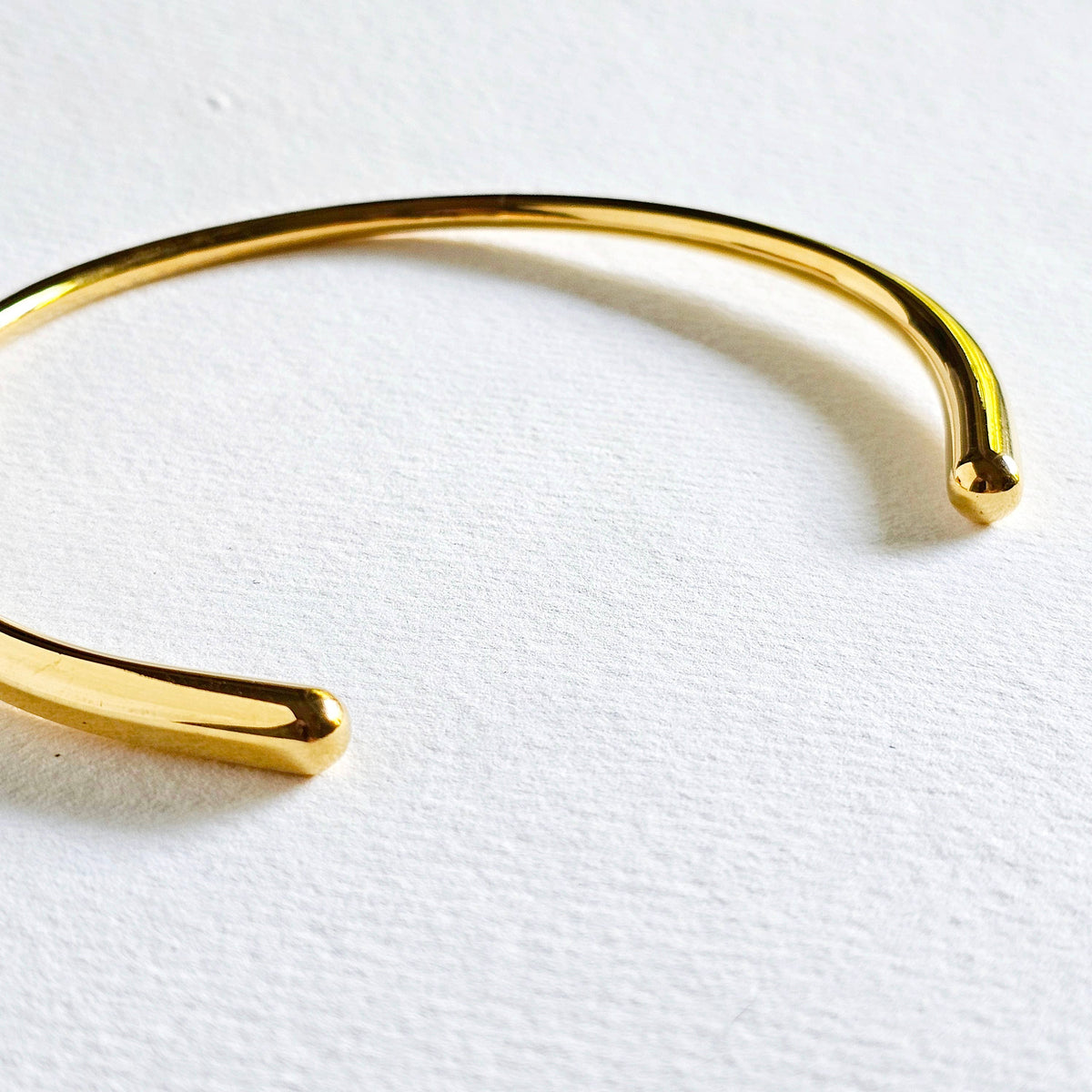 A polished gold minimalist style collar necklace resting on a textured white surface.